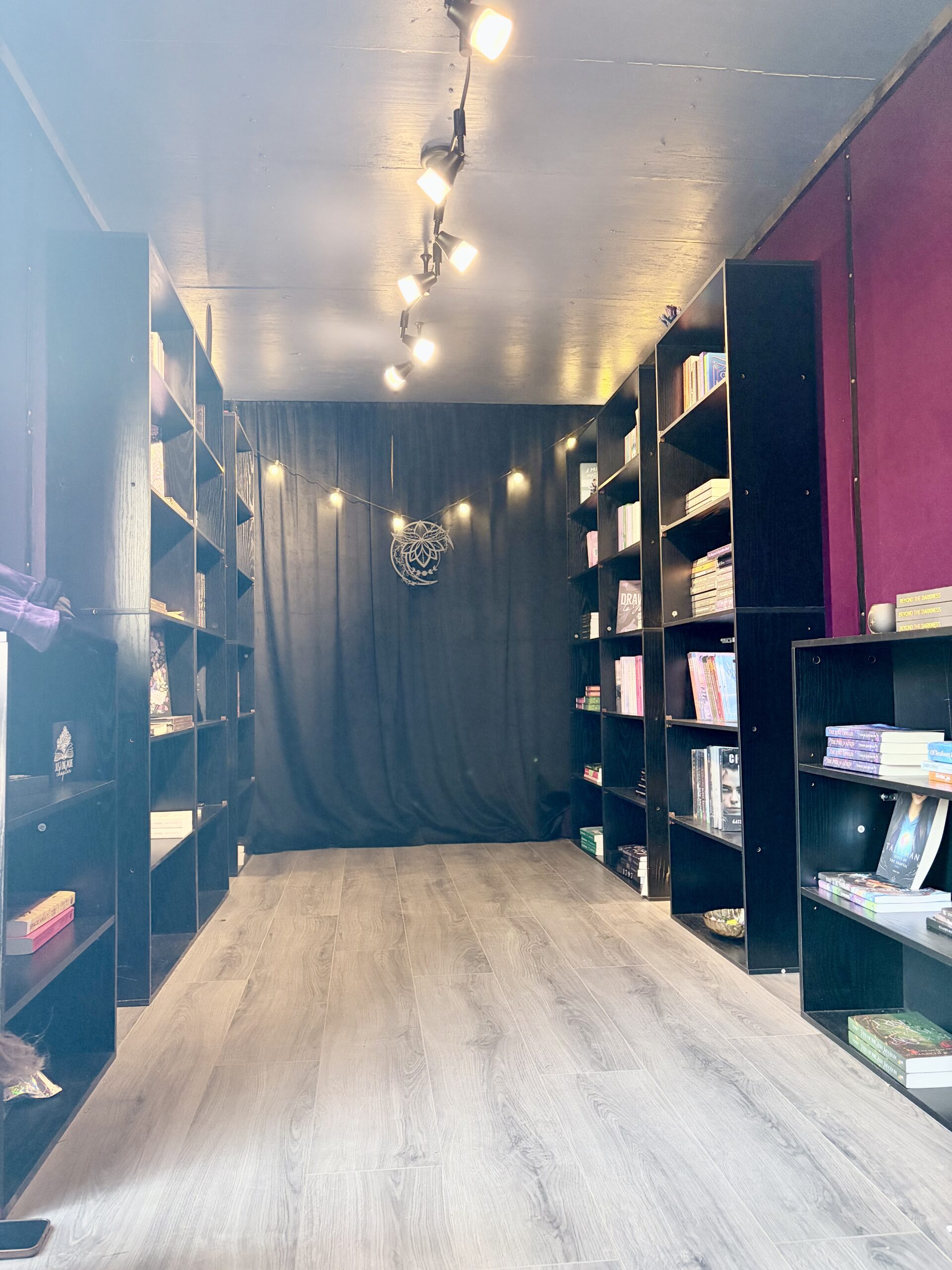 Interior of the Midnight Haven Books mobile bookshop, with black bookshelves, warm lighting, and plum walls